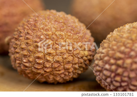 ripe red lychees scattered on a wooden table, red-skinned lychee fruits,rough textured lychee peel closeup 133101781
