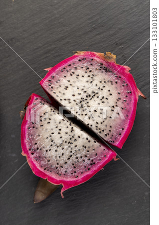 on pitaya cut in half with lots of small black seeds and white soft sweet flesh inside, sweet ripe dragon fruit with black small seeds and light flesh cut in half 133101803
