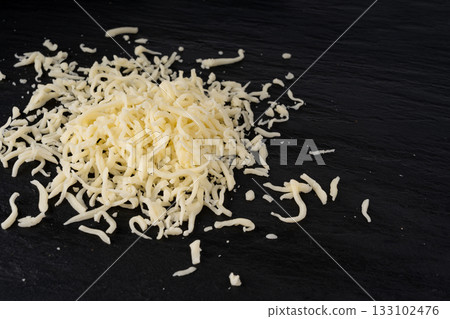 Grated mozzarella cheese on black background. Shredded mozarella texture Grated mozzarella cheese on black background. Shredded mozarella texture 133102476