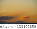 A sunset sky with an ascending and turning airplane flying 133102859