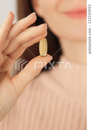 Close-up of an unrecognizable woman holding a fish oil capsule, promoting daily supplement and heart health. Close-up of an unrecognizable woman holding a fish oil capsule, promoting daily supplement and heart health. 133103052