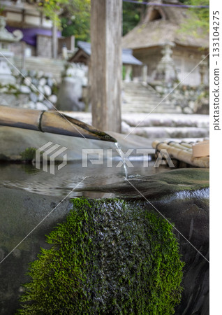 Pure spring water dripping from the chozuya (purification fountain) at Shirakawa Hachiman Shrine in Shirakawa-go, and moss-covered stones 133104275