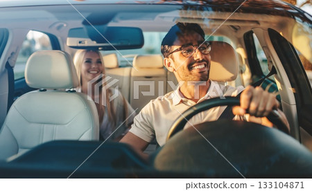 Joyful Driver with Glasses and Smiling Passenger Enjoying Sunny Road Trip Adventure in Modern Vehicle Interior 133104871