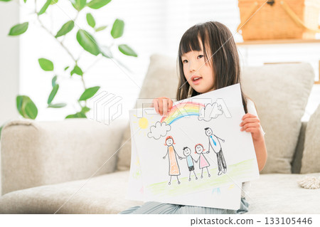 A girl showing off a drawing she made on the living room sofa 133105446