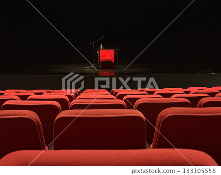 Stage with microphone and table seen from audience seats. Anticipation, art, and human expression through minimal lighting and quiet space. Stage with microphone and table seen from audience seats. Anticipation, art, and human expression through minimal lighting and quiet space. 133105558