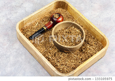 Smoking pipe with tobacco on a table. Smoking pipe with tobacco on a table. 133105975