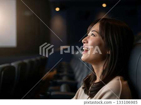 A woman laughing while watching a movie at the cinema 133106985
