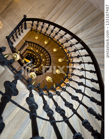Spiral staircase with ornate railing and warm hanging lamps viewed from above Spiral staircase with ornate railing and warm hanging lamps viewed from above 133107487