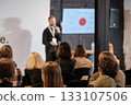 Speaker presenting at a conference to a seated audience with a presentation screen 133107506