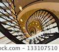 Spiral staircase view from above with ornate railings and warm hanging lights creates depth 133107510