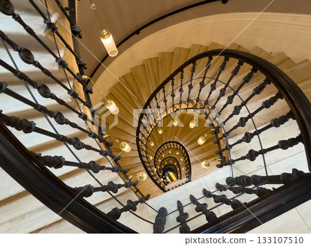 Spiral staircase view from above with ornate railings and warm hanging lights creates depth Spiral staircase view from above with ornate railings and warm hanging lights creates depth 133107510