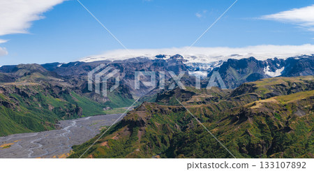 A winding river in Iceland flows through a lush green valley surrounded by cliffs, with a massive glacier in the background under a clear blue sky. A winding river in Iceland flows through a lush green valley surrounded by cliffs, with a massive glacier in the background under a clear blue sky. 133107892
