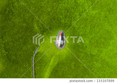 An aerial view shows a small airplane on a gravel clearing surrounded by vibrant green grass, with a faint path leading to the aircraft in Iceland. 133107899