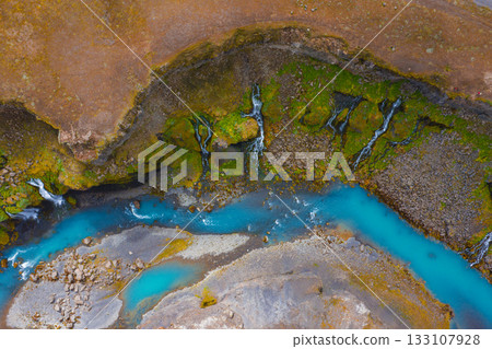 Aerial view of Sigoldugljufur Canyon in Iceland, featuring a turquoise river, moss covered cliffs, and cascading waterfalls amid rugged terrain. 133107928