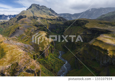 Mulagljufur Canyon in Iceland features steep mossy cliffs, a winding river, and a prominent mountain under a partly cloudy sky with diffused light. Mulagljufur Canyon in Iceland features steep mossy cliffs, a winding river, and a prominent mountain under a partly cloudy sky with diffused light. 133107934