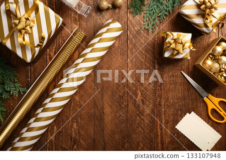 Flat lay of gold and white striped wrapping paper, ribbon, scissors, and small gift boxes on wooden table. Christmas gift wrapping. Copy space. 133107948