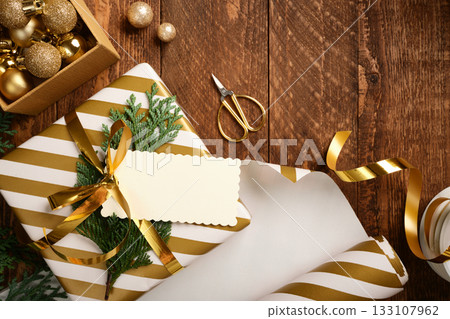 Christmas golden and white gift box with blank rectangular tag on wooden background. Copy space 133107962