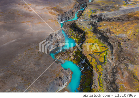 Aerial view of Sigoldugljufur Canyon in Iceland, featuring a turquoise river winding through steep rocky walls with green moss and earthy terrain. Aerial view of Sigoldugljufur Canyon in Iceland, featuring a turquoise river winding through steep rocky walls with green moss and earthy terrain. 133107969
