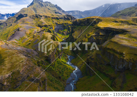 Mulagljufur Canyon in Iceland features steep moss covered cliffs, a winding river, rugged peaks, and patches of greenery under soft natural light. Mulagljufur Canyon in Iceland features steep moss covered cliffs, a winding river, rugged peaks, and patches of greenery under soft natural light. 133108042