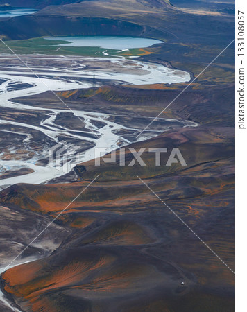 Aerial view of a braided river winding through a valley with vibrant orange and brown hills, a turquoise lake, and green vegetation in Iceland. Aerial view of a braided river winding through a valley with vibrant orange and brown hills, a turquoise lake, and green vegetation in Iceland. 133108057