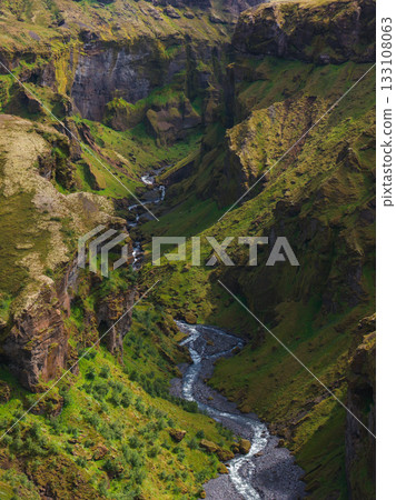 Aerial view of Mulagljufur Canyon in Iceland, featuring a winding river, steep moss covered cliffs, and vibrant vegetation under dynamic lighting. Aerial view of Mulagljufur Canyon in Iceland, featuring a winding river, steep moss covered cliffs, and vibrant vegetation under dynamic lighting. 133108063