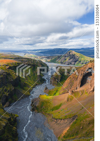 Aerial view of Mulagljufur Canyon in Iceland, featuring a winding river, steep cliffs with green vegetation, and distant mountains under a cloudy sky. Aerial view of Mulagljufur Canyon in Iceland, featuring a winding river, steep cliffs with green vegetation, and distant mountains under a cloudy sky. 133108064