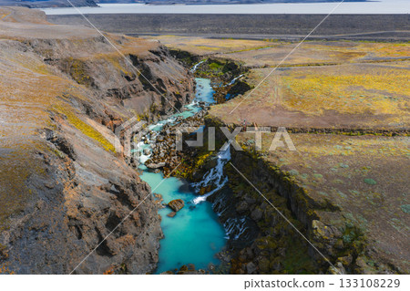 Turquoise river winds through Sigoldugljufur Canyon in Iceland, with small waterfalls, moss covered rocks, and a distant flat expanse in the background. Turquoise river winds through Sigoldugljufur Canyon in Iceland, with small waterfalls, moss covered rocks, and a distant flat expanse in the background. 133108229