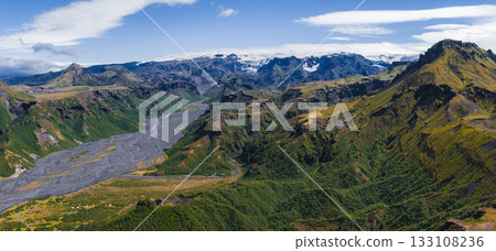 Aerial view of a glacial river winding through a green valley in Iceland, surrounded by dramatic mountains and snow capped peaks under a partly cloudy sky. Aerial view of a glacial river winding through a green valley in Iceland, surrounded by dramatic mountains and snow capped peaks under a partly cloudy sky. 133108236