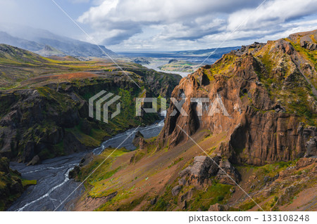 Mulagljufur Canyon in Iceland features dramatic cliffs, vibrant green vegetation, a winding river, rugged rock formations, and a cloudy sky. 133108248