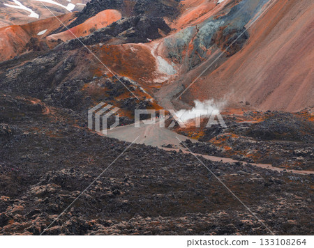 Vibrant rhyolite hills and volcanic terrain in Iceland, with a steaming geothermal vent and hikers adding scale to the dramatic environment. 133108264