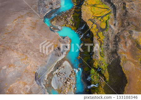 Turquoise river flows through a rugged canyon in Iceland, surrounded by earthy brown terrain, green moss, and cascading waterfalls. Turquoise river flows through a rugged canyon in Iceland, surrounded by earthy brown terrain, green moss, and cascading waterfalls. 133108346