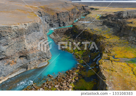 The Sigoldugljufur canyon in Iceland features a turquoise river, steep rocky cliffs, mossy vegetation, small waterfalls, and a barren landscape. 133108383