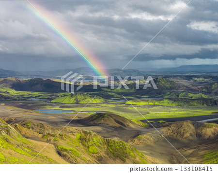 Aerial view of Iceland's green moss covered hills, volcanic soil, lakes, and streams, with a vivid rainbow under dramatic cloudy skies. Aerial view of Iceland's green moss covered hills, volcanic soil, lakes, and streams, with a vivid rainbow under dramatic cloudy skies. 133108415