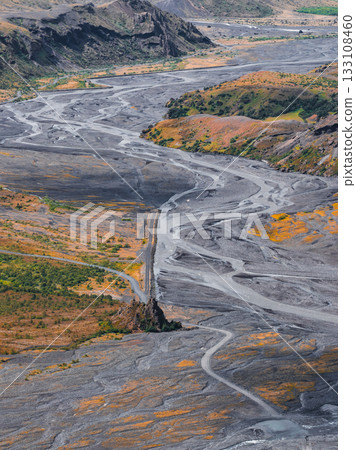 Aerial view of a braided river flowing through volcanic soil and green vegetation in Iceland, with steep rocky cliffs in the background. Aerial view of a braided river flowing through volcanic soil and green vegetation in Iceland, with steep rocky cliffs in the background. 133108460