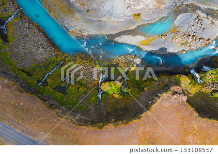 Turquoise river winds through rugged Icelandic landscape near Sigoldugljufur canyon, bordered by moss covered terrain and cascading waterfalls. 133108537