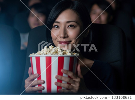 一位女士一邊看電影一邊拿著爆米花桶 133108681