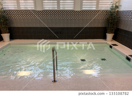 Modern spa interior featuring a tranquil thermal pool with rippling water and a stainless steel handrail Modern spa interior featuring a tranquil thermal pool with rippling water and a stainless steel handrail 133108782