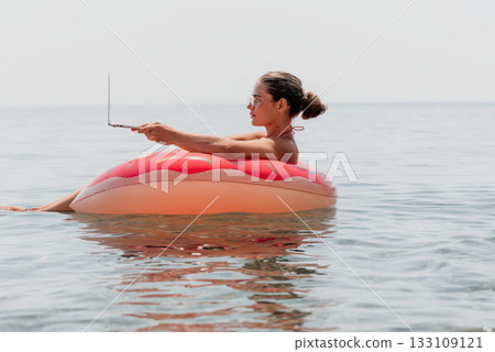 Woman Laptop Beach - Working on Laptop While Floating on an Inflatable Ring in the Ocean. Woman Laptop Beach - Working on Laptop While Floating on an Inflatable Ring in the Ocean. 133109121