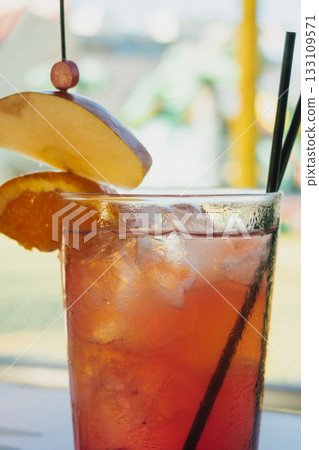 Refreshing non-alcoholic strawberry Mojito cocktail served in a sweaty glass with ice and garnished with apple and orange slices. Close-up on a bright summer patio background Refreshing non-alcoholic strawberry Mojito cocktail served in a sweaty glass with ice and garnished with apple and orange slices. Close-up on a bright summer patio background 133109571