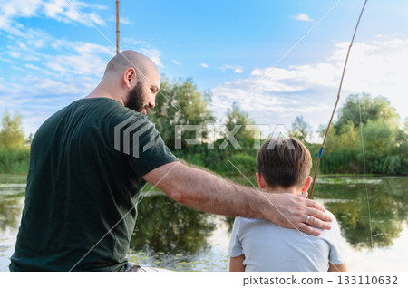 Father with hand on sons back while fishing by river. Father with hand on sons back while fishing by river. 133110632