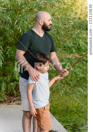 Father guiding young son holding fishing rod outdoors 133110636
