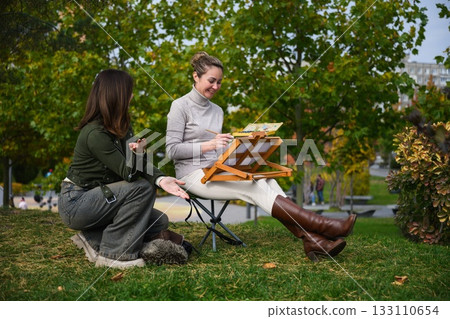 Two women talking while painting outdoors in park. Two women talking while painting outdoors in park. 133110654