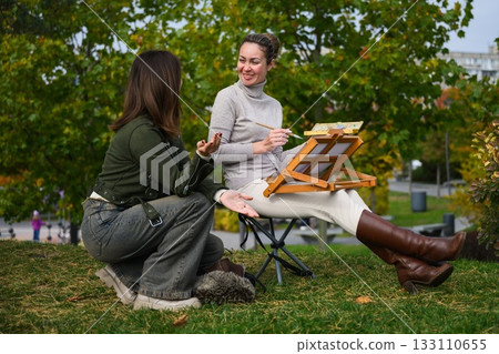 Two women talking while painting outdoors in park. Two women talking while painting outdoors in park. 133110655