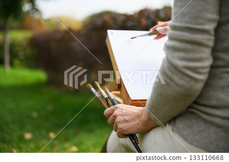 Close-up of artist painting on blank canvas outdoors. 133110668