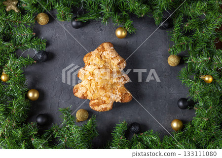 Festive christmas tree pastry with almonds surrounded by pine and baubles on dark stone background 133111080