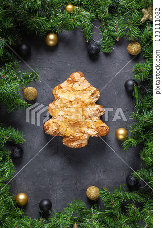Festive christmas tree pastry with almonds surrounded by pine and baubles on dark stone background Festive christmas tree pastry with almonds surrounded by pine and baubles on dark stone background 133111082