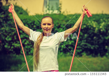 Girl doing exercises outdoor, using resistance fit band. Girl doing exercises outdoor, using resistance fit band. 133111343