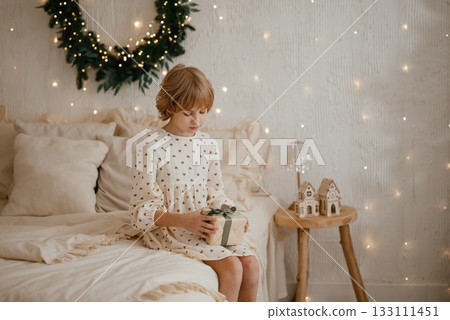 Child Sitting on Bed with Christmas Gift in Cozy Room 133111451