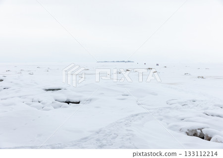A tranquil winter shoreline blanketed in snow stretches to a pale horizon A tranquil winter shoreline blanketed in snow stretches to a pale horizon 133112214