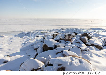 Snow covered rocks dominate the foreground of a quiet, frozen shoreline Snow covered rocks dominate the foreground of a quiet, frozen shoreline 133112219
